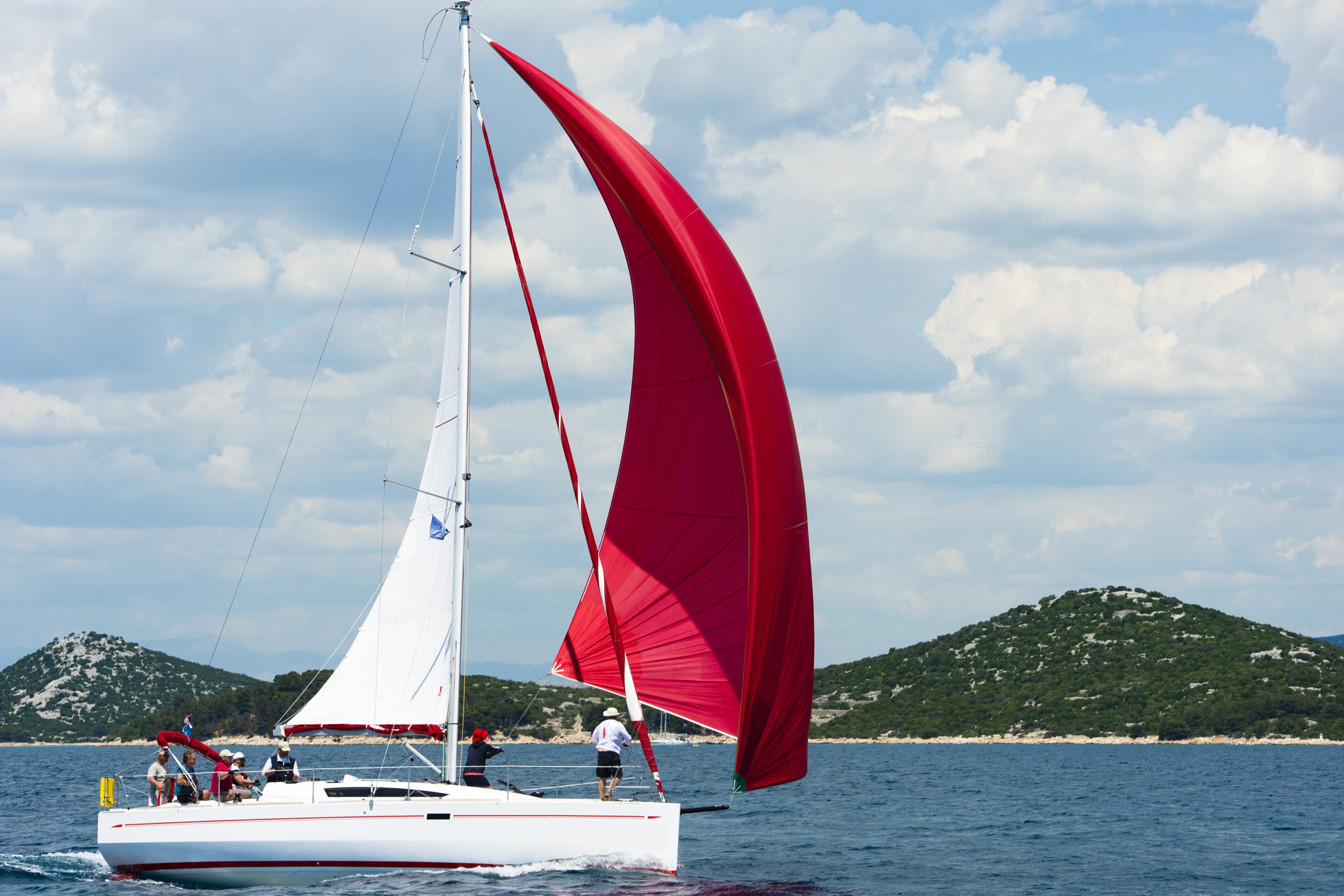 Side view of beautiful sailboat using white main sail and red genacker